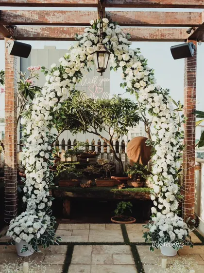 A lush and rustic floral arch made entirely of white flowers frames this beautiful rooftop proposal space. The natural wood of the pergola combined with the elegant white decor creates a stunning contrast.