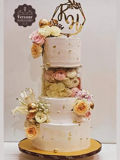 A stunning three-tier wedding cake with a separator filled with flowers. The design is elegant and romantic, with gold leaf accents and a custom initial topper for the couple.
