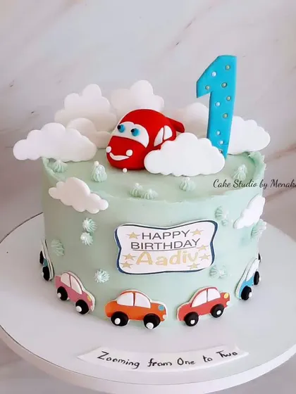 A super cute car themed cake for a first birthday. This design features a friendly red car zooming from one to two, surrounded by fluffy clouds.