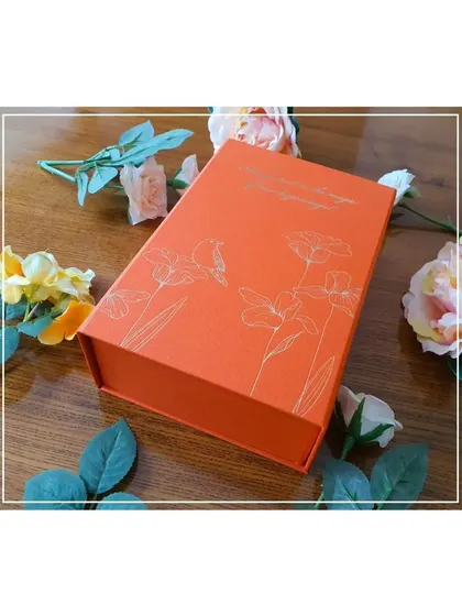 A close-up of the custom orange box with gold foil detailing. Creating a fully bespoke container adds an extra layer of luxury and thoughtfulness to the invitation suite.