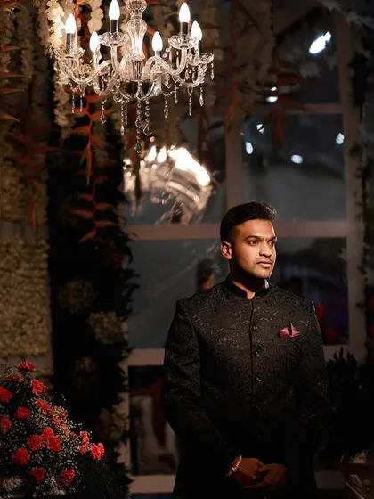 A handsome portrait of the groom at his reception, looking dapper against a backdrop of flowers and a crystal chandelier.