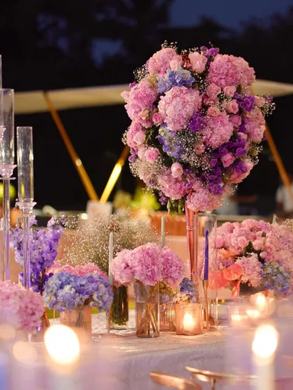 A beautiful composition of pink and lavender hydrangeas, creating a soft and dreamy centerpiece. The blurred candlelight in the foreground adds to the romantic and ethereal mood of the evening.