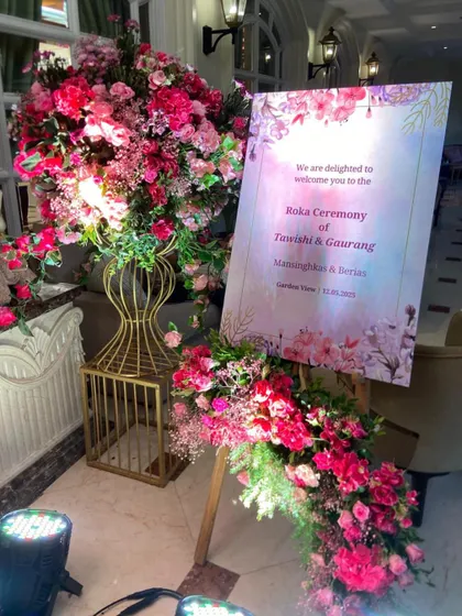 A beautiful welcome easel for a Roka ceremony, adorned with lush arrangements of pink flowers, setting a warm and inviting tone for the event.