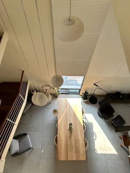 An overhead view of the dining area in the Jayanagar Residence, situated within a double-height space. A large skylight and a cluster of pendant lights ensure the area is bright and welcoming at all times.