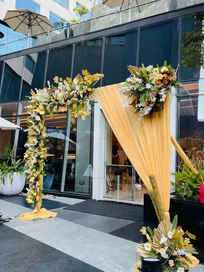 A modern and asymmetrical entrance decoration outside a hotel. The setup uses golden drapes and beautiful floral arrangements for a chic and welcoming look.