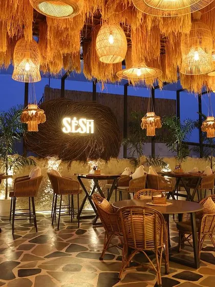The bar and seating area at Sesh, where a canopy of hanging straw and bamboo light fixtures creates a warm, bohemian atmosphere against the evening sky.