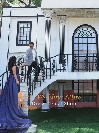 A couple on a grand staircase. The woman's dark blue gown trails behind her, adding a touch of elegance and drama to the architectural setting.