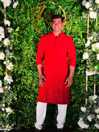 Posing in a classic red kurta against a beautiful floral backdrop at a sangeet event.