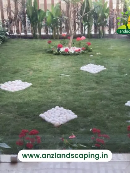 A courtyard garden viewed through glass panels, featuring a central tree, floral arrangements, and decorative white pebble stepping stones on the lawn.