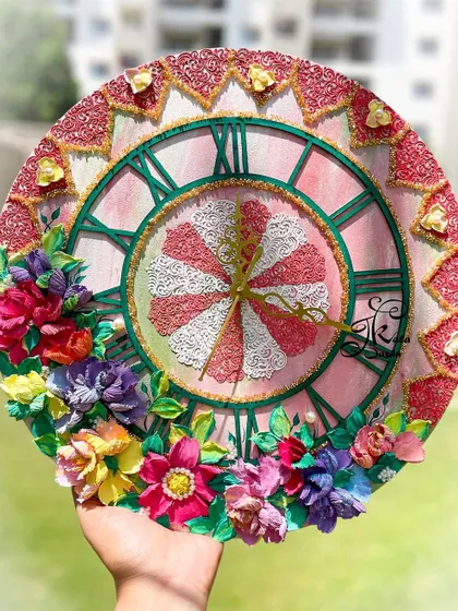 A 16-inch wall clock with a lovely pink-themed base and a contrasting green dial. The piece is adorned with multi-colored flowers and small heart details.