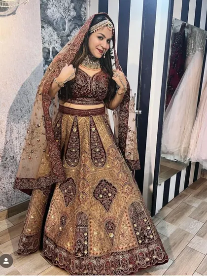 A client trying on a complete bridal look in my store. This maroon and gold embroidered lehenga is paired with a matching choker, maang tikka, and earrings, ready for her big day.