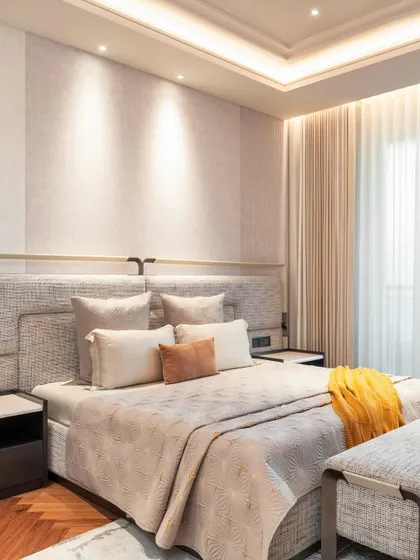 This bedroom design uses integrated lighting in the headboard and ceiling to create a warm, ambient glow. The yellow throw adds a pop of color to the otherwise neutral and calming palette.