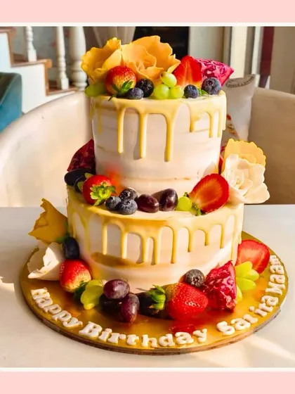 A fresh two-tier fruit drip cake, perfect for a sunny celebration, adorned with various fresh fruits.