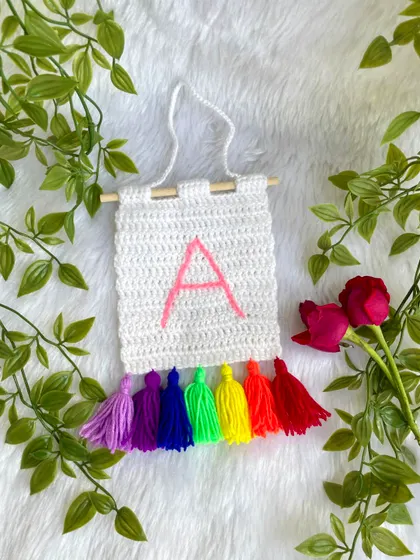 I make these personalized initial banners, perfect for a nursery or a child's room door. This one features the letter 'A' with a vibrant rainbow of tassels.