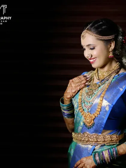 A classic studio-style portrait of the bride against a dark background, making her vibrant blue saree and gold jewelry stand out.