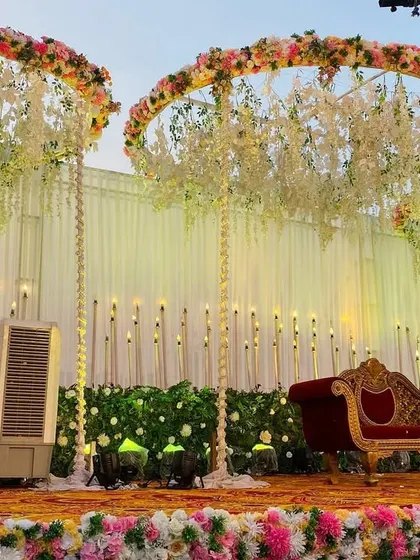 An elegant reception stage with three large, suspended floral rings and a backdrop of warm lights. The red velvet sofa adds a classic touch.