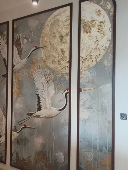 This is a custom three-panel art piece created with wallpaper. The design of cranes against a textured moon is framed with dark wood moulding for a sophisticated, Japanese-inspired look.