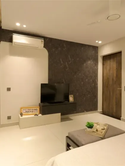 The TV unit in this monochrome bedroom features a stepped design with stone veneer and black textured laminate, adding depth and character.
