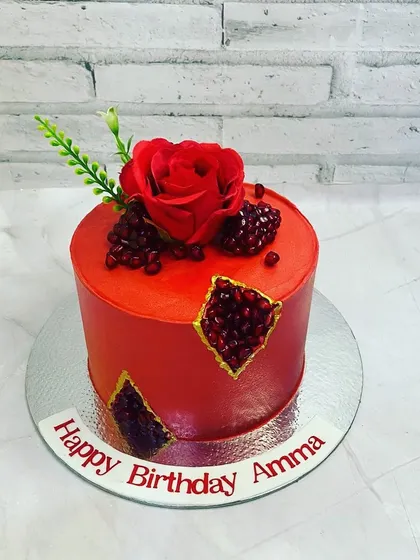 A gorgeous red cake for a mother's birthday. The design features a geode-style cutout filled with edible pomegranate seeds and is topped with a fresh red rose.
