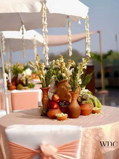 A charming tabletop setup with earthen pots filled with fresh fruits, betel leaves, and jasmine flowers, celebrating nature and cultural richness.