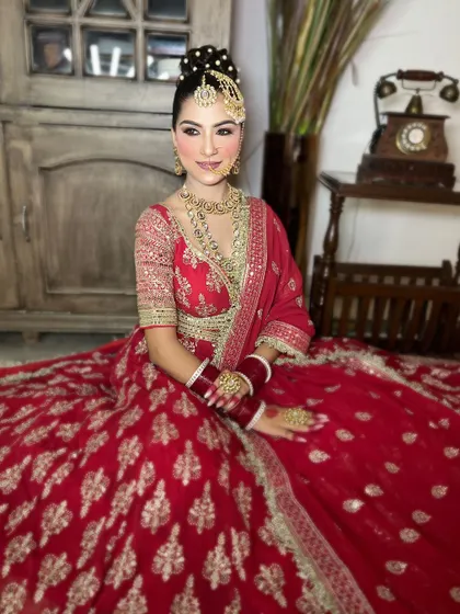 A full-length seated shot displaying the beautiful flare of a red and gold embroidered lehenga, perfect for capturing regal bridal portraits.