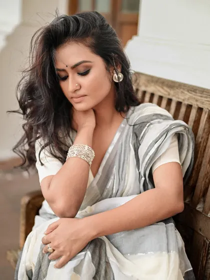A thoughtful, seated portrait for AVA India. The model's relaxed pose on a wooden bench creates a relatable and gentle image, perfect for showcasing wearable art.