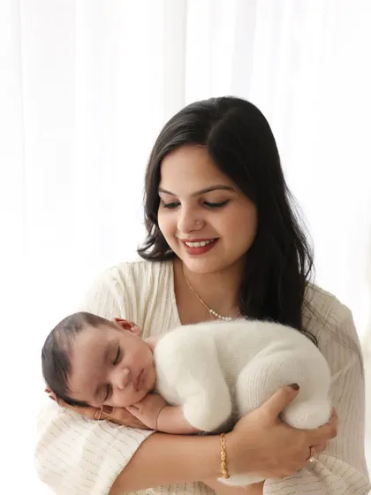 A beautiful solo portrait of a mother cradling her newborn. The baby is snug in a soft, fuzzy white outfit, emphasizing their newness and innocence.