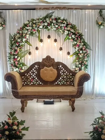 A modern engagement stage with a floral arch and hanging industrial-style bulbs.