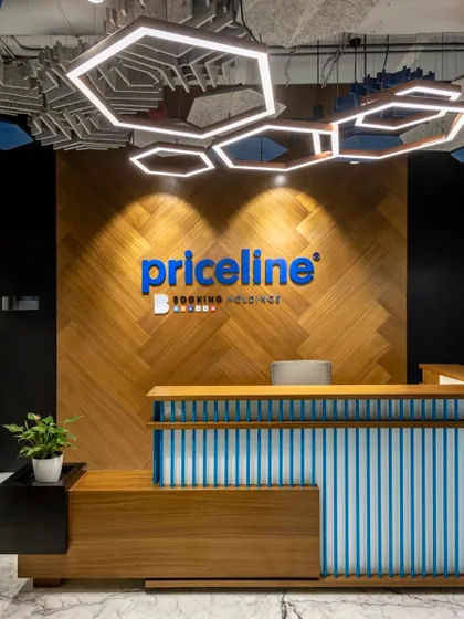 The reception area we designed for Priceline, a Booking Holdings company. The design features a custom reception desk, chevron wood paneling, and a striking hexagonal lighting fixture, creating a memorable and professional first impression.