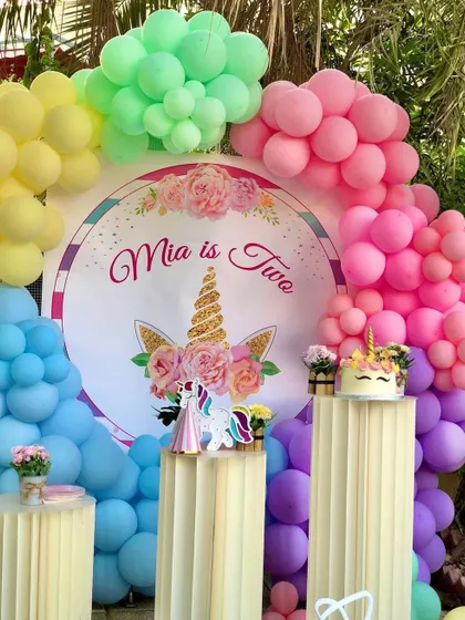 A vibrant unicorn theme with a rainbow balloon arch. The setup includes a custom backdrop and themed cake stands, perfect for a colorful and cheerful birthday party.