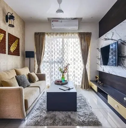 A cozy living room setup featuring a dark wood media unit with a striking white marble-patterned laminate backdrop. The warm tones of the curtains and sofa create an inviting space for family movie nights.