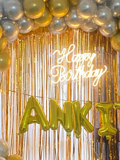 The glowing neon sign against the shimmering gold fringe curtain creates a glamorous and festive photo opportunity.