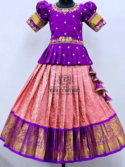 A peplum lehenga in a classic pink and purple combination. The purple blouse has delicate embroidery, and the pink Banarasi skirt is finished with a traditional purple and gold border.