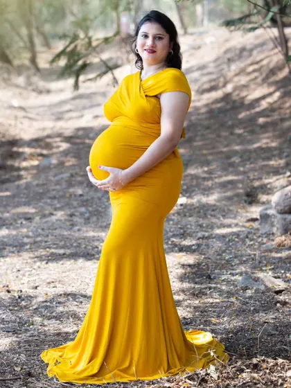 This portrait showcases a classic pose for maternity photography, with the mother-to-be gently holding her baby bump. The natural, rustic background helps to keep the focus entirely on her, celebrating this special time in a simple and beautiful way.