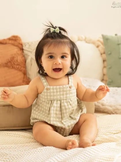 Her smile lights up the whole room! This happy baby girl in a gingham romper is the perfect example of a joyful sitter session.