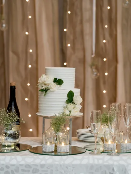A classic white two-tiered cake on a table decorated with fairy lights and candles, creating a simple and romantic dessert corner.