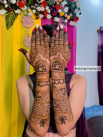 A happy bride showing off her full-arm mehndi against a colorful backdrop. This design is packed with traditional patterns, perfect for a vibrant sangeet or wedding ceremony.