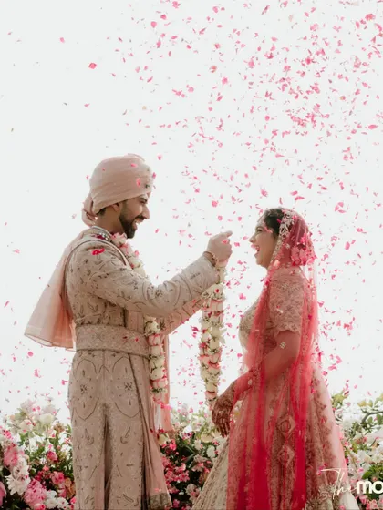 A moment of pure, unscripted laughter during the varmala ceremony. The shower of pink petals adds to the joy and spontaneity of this beautiful candid shot.