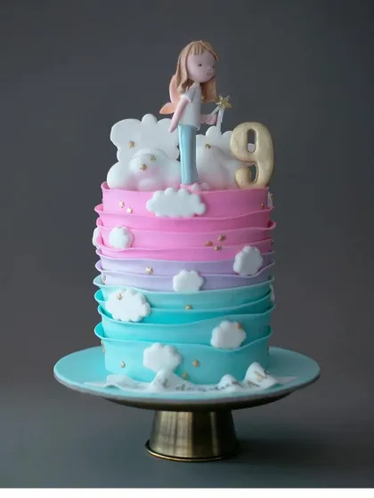 A dreamy pastel ombre cake for a 9th birthday. The soft transition from pink to blue is accented with fluffy clouds and a simple figurine.