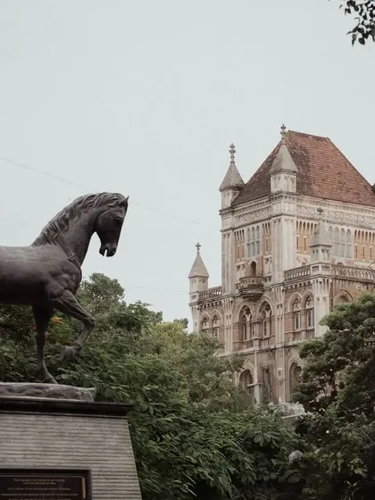 A series of photographs capturing the architectural memory of old Bombay. These images feature landmarks like the Rajabai Clock Tower, the Asiatic Society Library, and other colonial-era structures, often framed by trees.