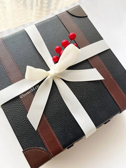 A luxury leather-finish trunk box tied with a simple white ribbon and a sprig of holly. This packaging is perfect for premium New Year and Christmas corporate gifts.