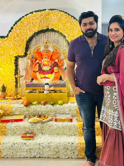 A happy client couple standing before their beautiful yellow floral Ganpati mandap. The traditional color scheme is perfect for creating a warm and festive atmosphere at home.