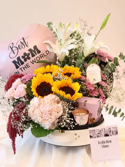 A full view of the sunflower and lily bouquet hamper. It's a cheerful and bright gift, complete with a "Best Mom in the World" balloon and a personalized card.