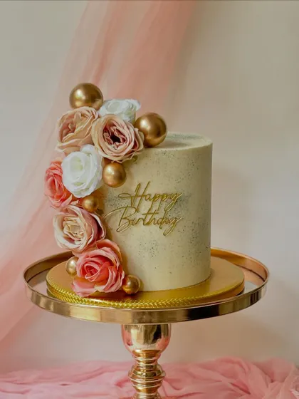 A beautiful birthday cake with a cascade of pink and cream roses and gold spheres. The custom gold "Happy Birthday" topper adds a personal touch.