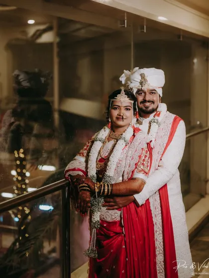 A classic wedding portrait of the couple by a railing, the bride in a stunning red saree, looking timeless and elegant.