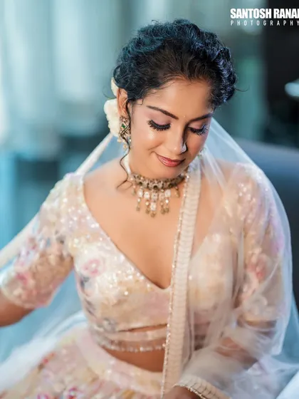 A gentle downward glance highlights the soft pink eyeshadow and the intricate details of the necklace and blouse.