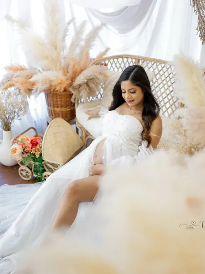 A dreamy and ethereal portrait. The mom-to-be is seated in a wicker chair, surrounded by soft clouds and pampas grass, creating a magical atmosphere.