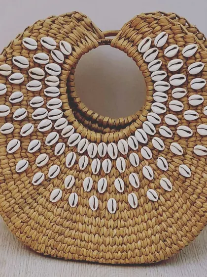 A stunning holiday bag made from woven seagrass and decorated with concentric circles of cowrie shells. This design is a must-have for beach resorts, gift shops, and fashion-forward customers.
