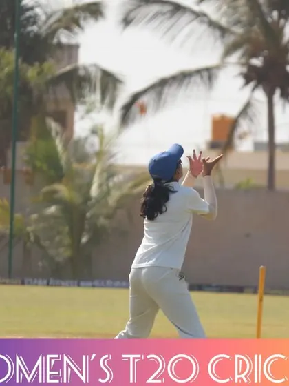 A fielder positions herself to take a high catch, with the umpire looking on.