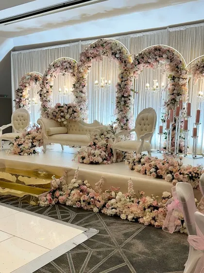 A true fairytale reception stage. The entire setup is a vision in pink and white, with multiple floral arches, elegant vintage furniture, and soft lighting.